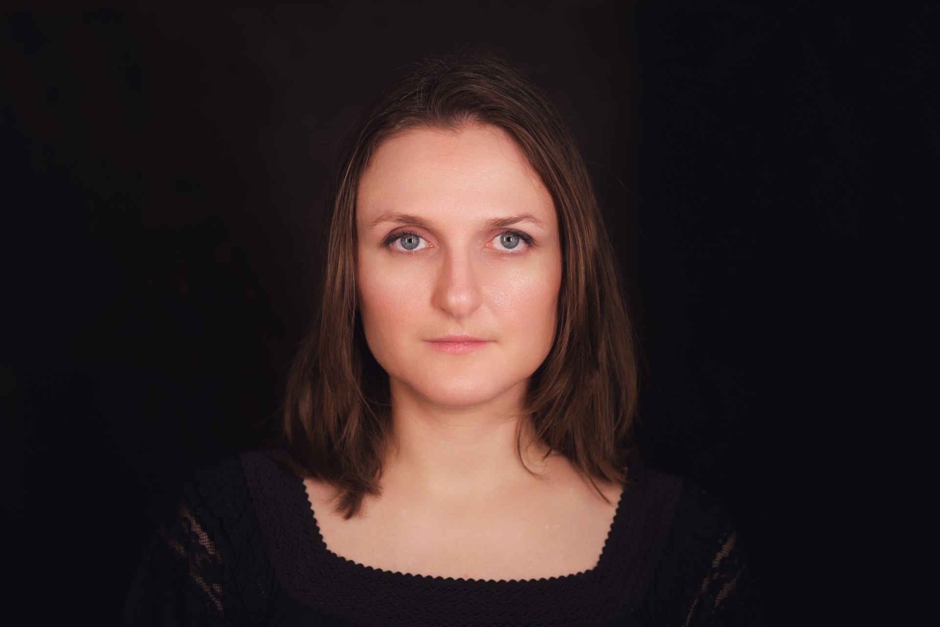 Studio portrait of a woman with brown hair wearing a black dress on a dark background. Professional headshot photography for design and print.